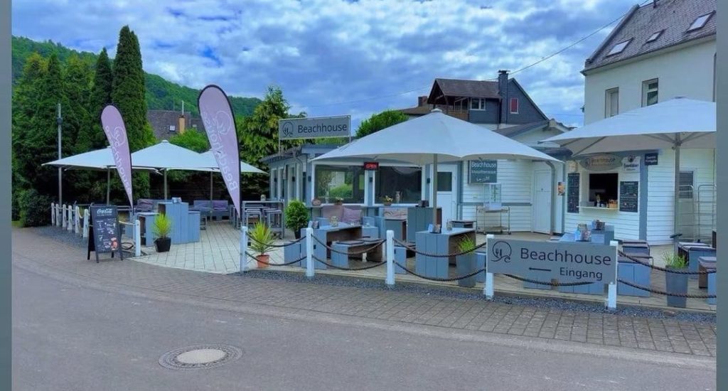 Außenansicht des Beachhouse mit Terrasse, Sonnenschirmen und Beachflags an der Straße