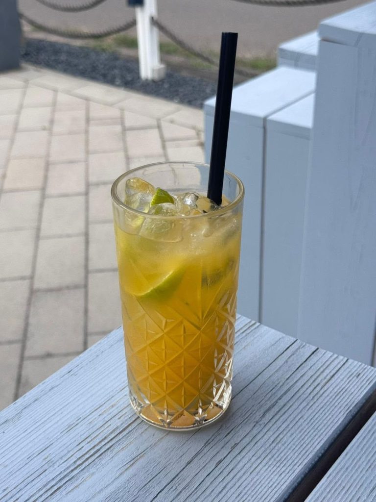 Gelber Longdrink mit Limette und Eis im Kristallglas auf der Terrasse des Beachhouse