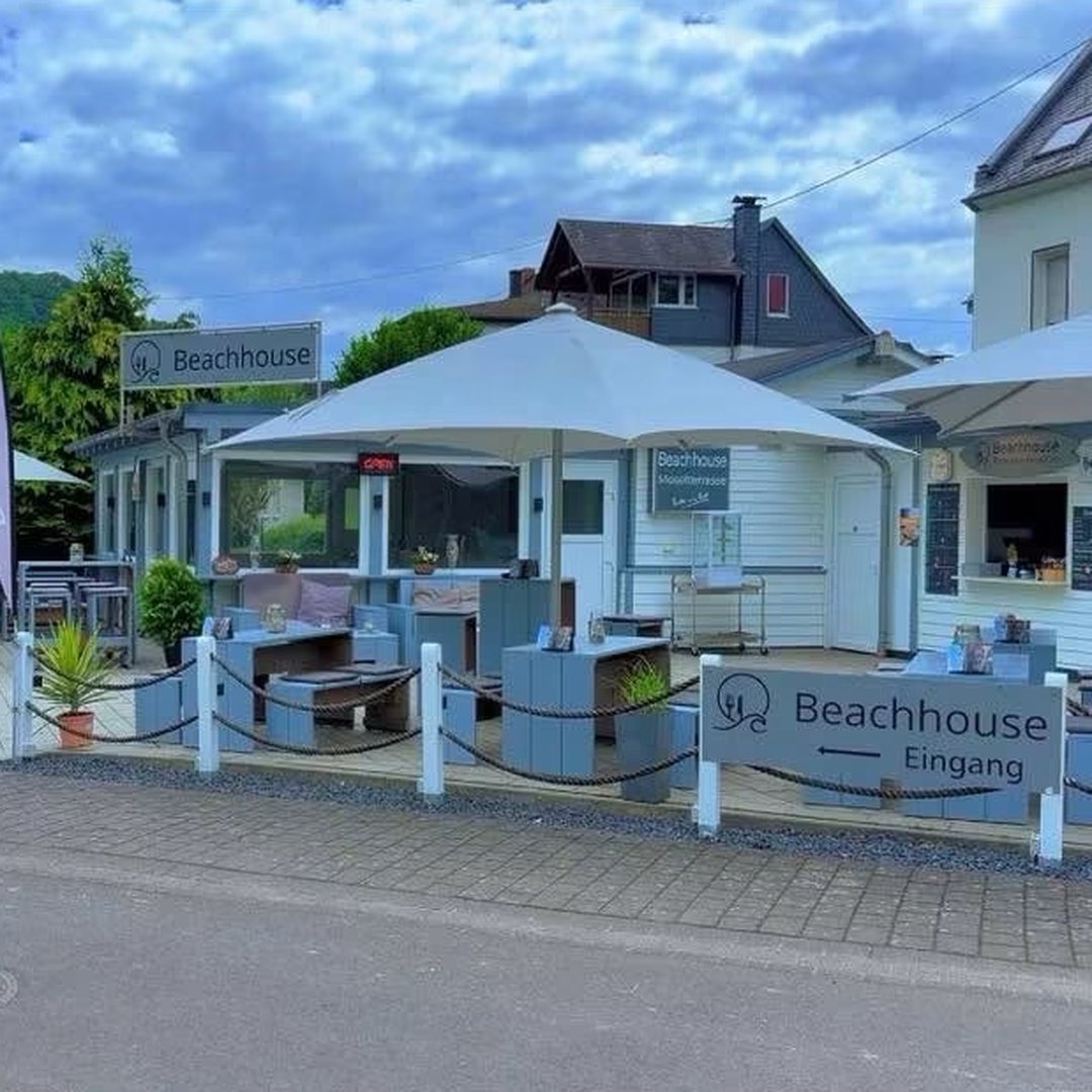 Das Beachhouse von der Straße aus: Kiosk mit Sonnenschirm, Terrasse und Schild zum Eingang